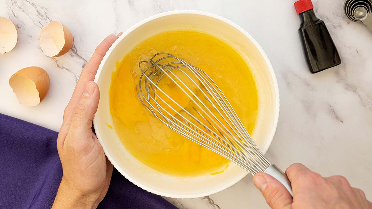 person beating eggs in a mixing bowl