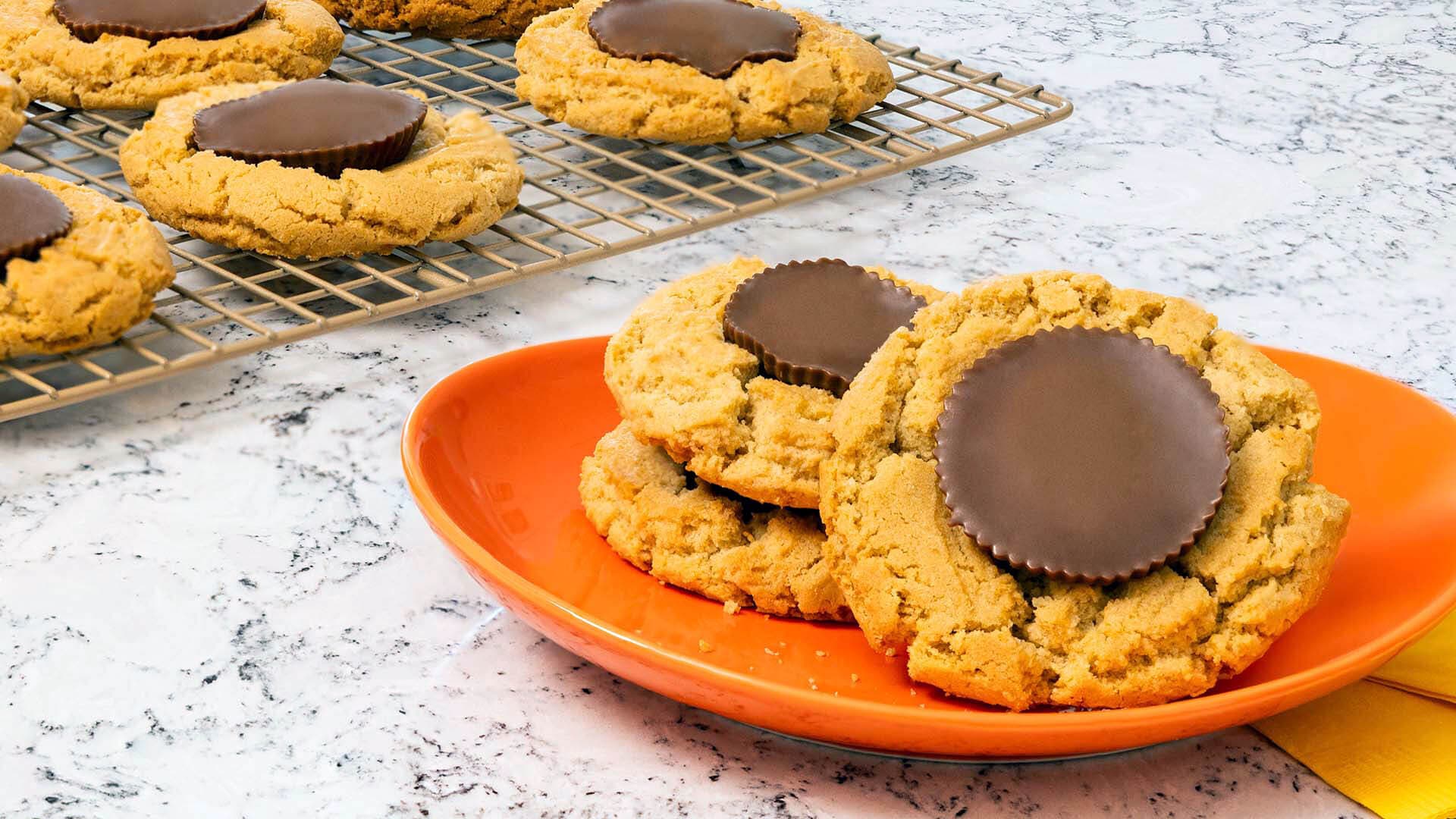 freshly bakes reeses peanut butter cup cookies stacked on plate and resting on cooling rack