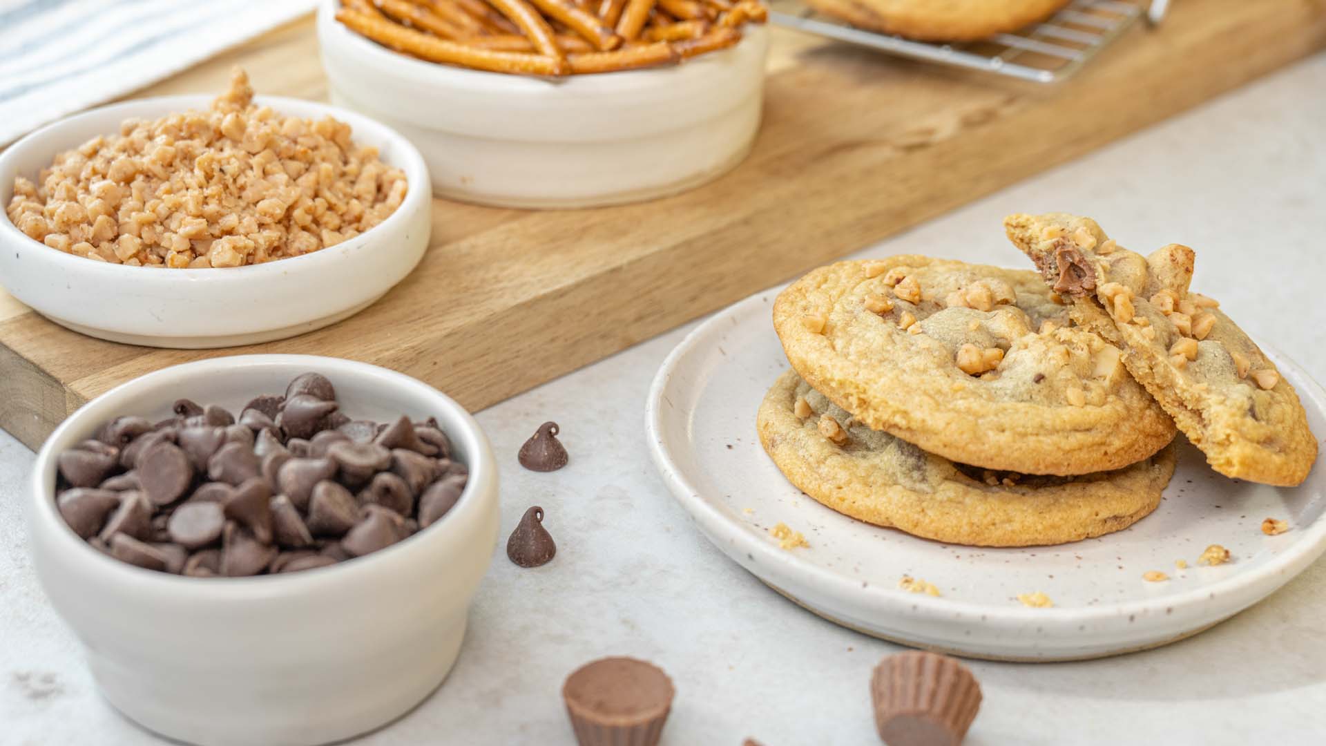plate of kitchen sink cookies beside bowls of baking chips, toffee bits, and pretzel sticks