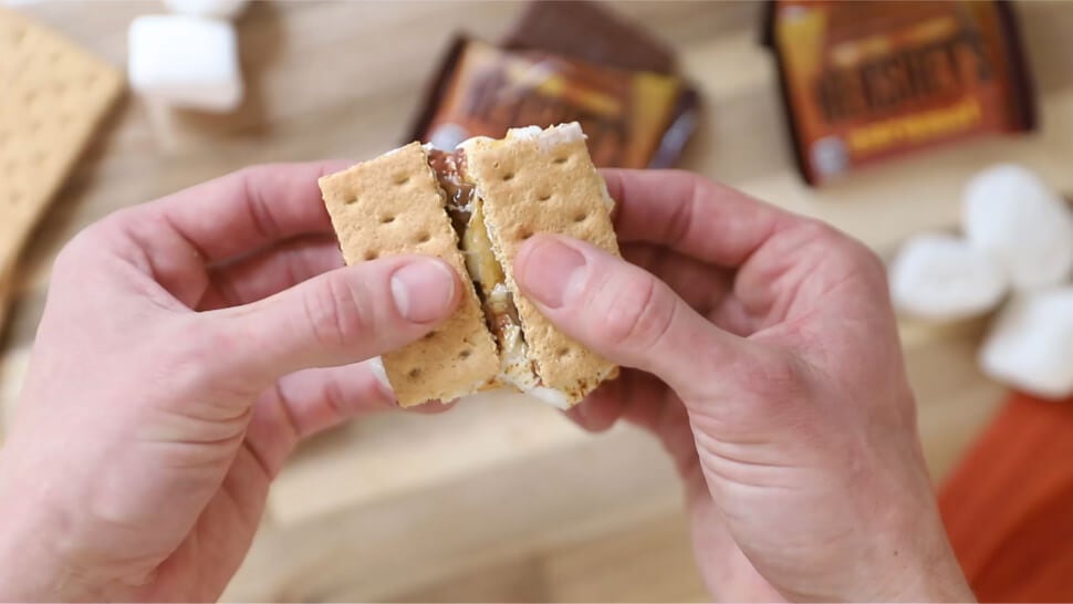 person breaking a hersheys milk chocolate with caramel flavored oven smore in half